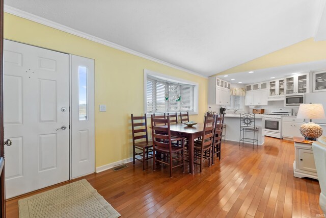 dining space with lofted ceiling, light wood-style flooring, baseboards, and ornamental molding