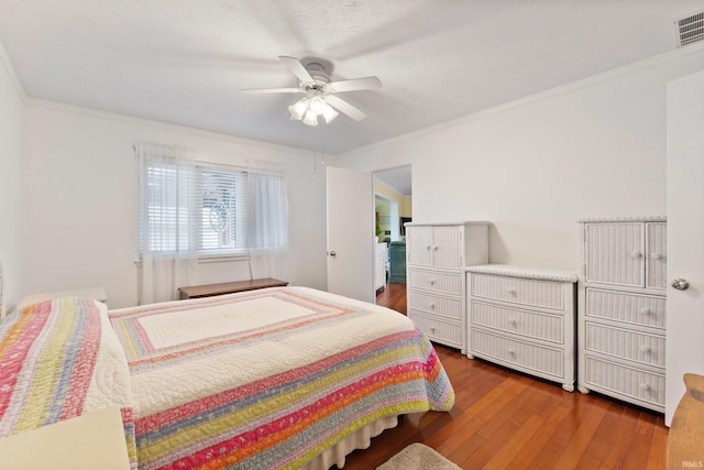 bedroom with a ceiling fan, crown molding, wood finished floors, and visible vents