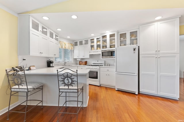 kitchen featuring white appliances, a peninsula, a sink, white cabinets, and light wood-style floors