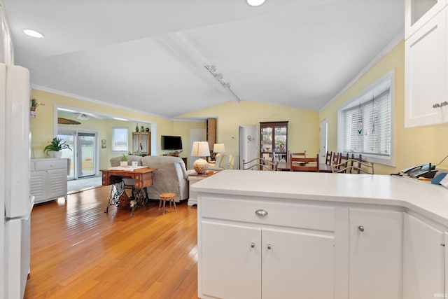 kitchen with lofted ceiling, light wood-style flooring, a peninsula, freestanding refrigerator, and white cabinetry