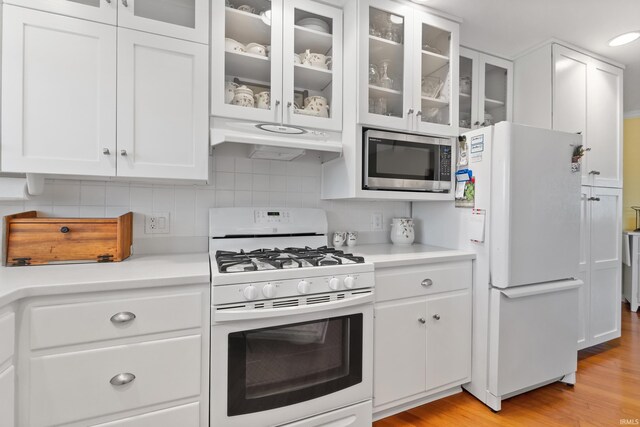 kitchen featuring white appliances, light countertops, white cabinets, under cabinet range hood, and backsplash