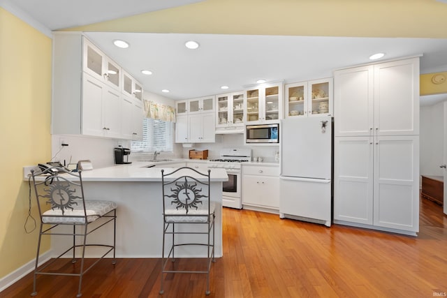 kitchen with white appliances, light wood finished floors, a peninsula, a sink, and a kitchen bar