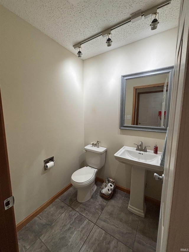 half bath with toilet, baseboards, and a textured ceiling