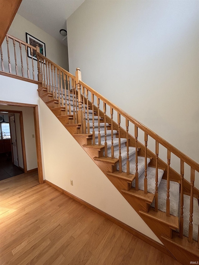 stairway with a high ceiling, baseboards, and wood finished floors