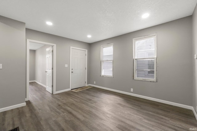 empty room featuring dark wood-type flooring, recessed lighting, baseboards, and a textured ceiling