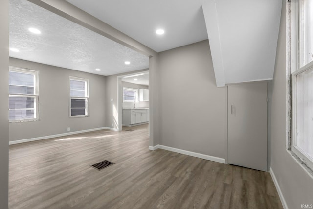 spare room with visible vents, a textured ceiling, baseboards, and wood finished floors