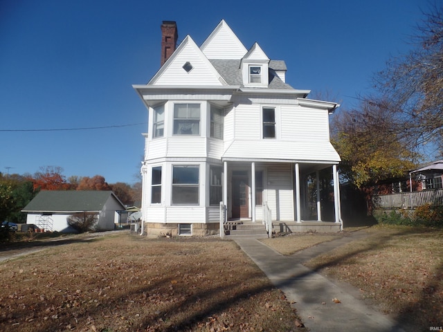 view of front of home featuring a chimney, a porch, a shingled roof, and a front yard