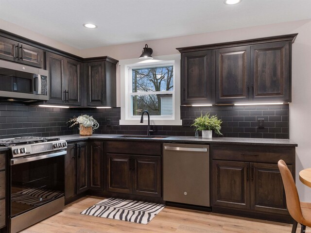 kitchen with light wood finished floors, dark countertops, dark brown cabinets, appliances with stainless steel finishes, and a sink