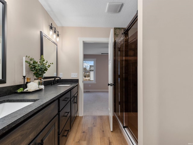 full bath featuring visible vents, double vanity, a stall shower, wood finished floors, and a sink