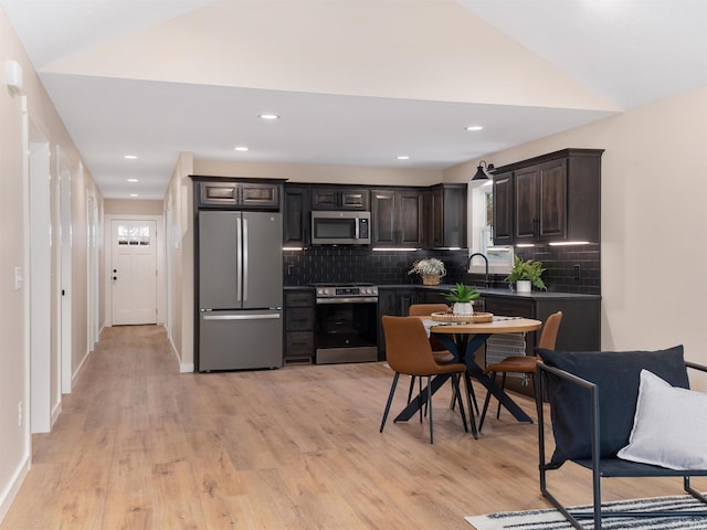 kitchen with tasteful backsplash, light wood-style floors, appliances with stainless steel finishes, dark brown cabinets, and vaulted ceiling