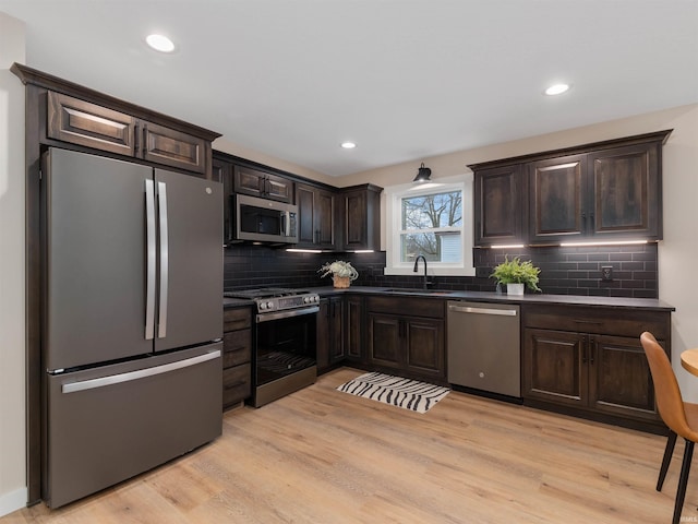 kitchen featuring a sink, dark countertops, dark brown cabinetry, appliances with stainless steel finishes, and light wood finished floors