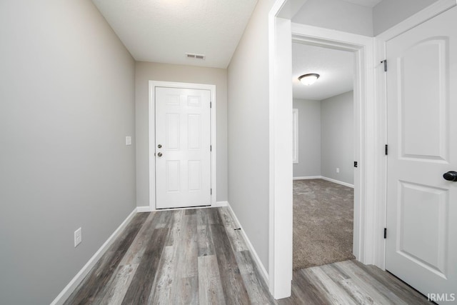 hallway with visible vents, baseboards, a textured ceiling, and wood finished floors