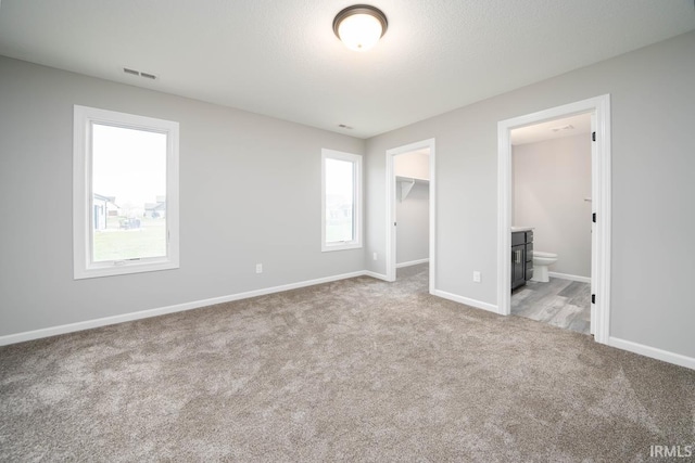 unfurnished bedroom featuring carpet flooring, a walk in closet, multiple windows, and baseboards