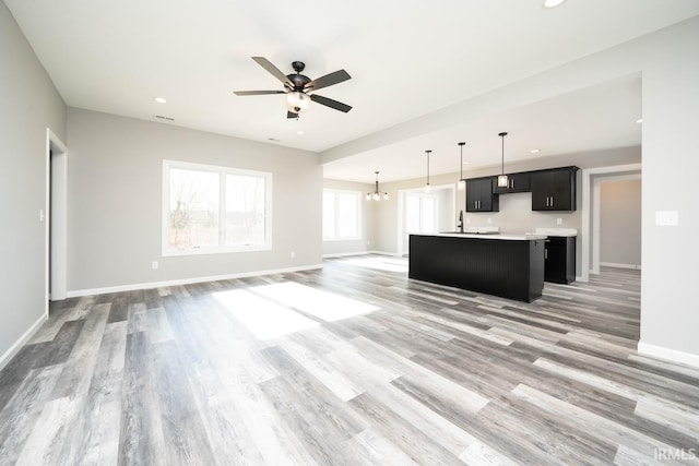 unfurnished living room featuring light wood finished floors, visible vents, baseboards, recessed lighting, and ceiling fan with notable chandelier