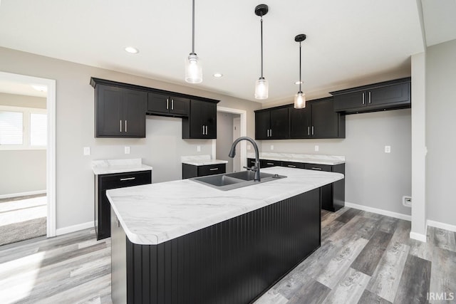 kitchen with a sink, baseboards, light wood-style floors, and a center island with sink