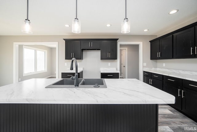 kitchen with a center island with sink, a sink, wood finished floors, dark cabinetry, and recessed lighting