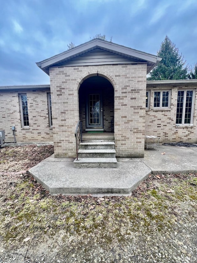 entrance to property with brick siding, central air condition unit, and a patio