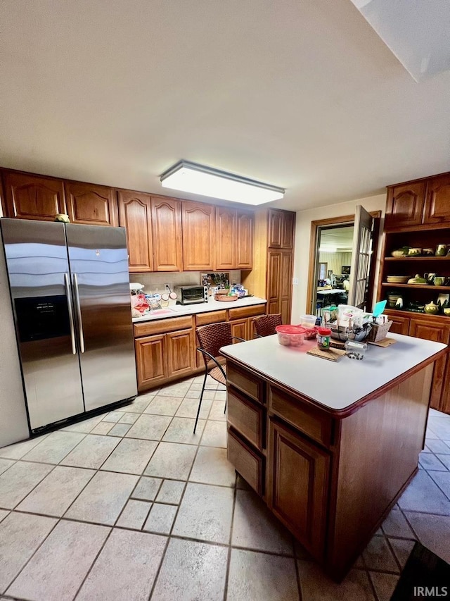 kitchen featuring a kitchen island, open shelves, stainless steel fridge with ice dispenser, light countertops, and brown cabinets