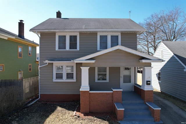 american foursquare style home with a shingled roof, fence, covered porch, and a chimney