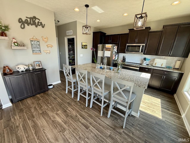 kitchen with a kitchen breakfast bar, stainless steel appliances, dark brown cabinetry, decorative backsplash, and dark wood-style flooring