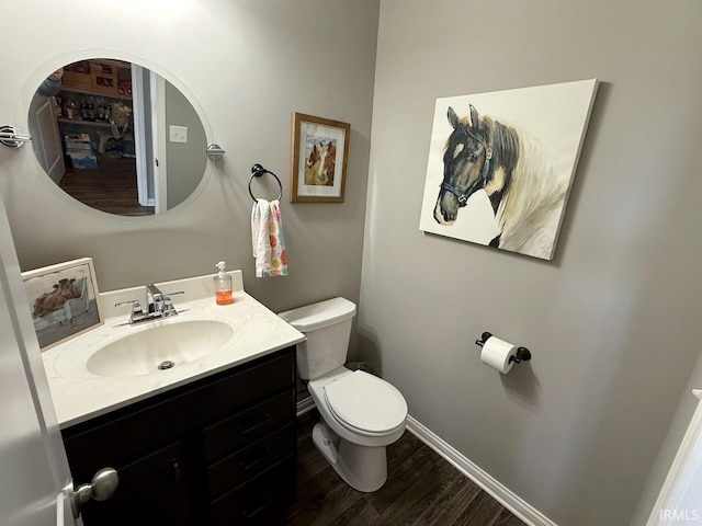 bathroom with toilet, vanity, baseboards, and wood finished floors