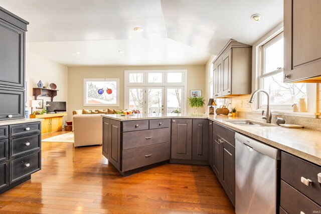 kitchen with a peninsula, a sink, wood-type flooring, dishwasher, and tasteful backsplash