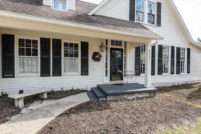 doorway to property featuring covered porch and roof with shingles