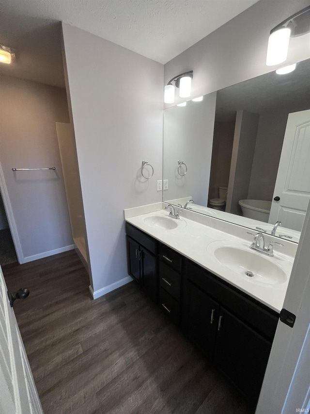 bathroom featuring baseboards, toilet, double vanity, wood finished floors, and a sink