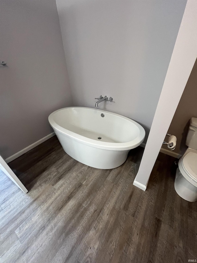 full bath with wood finished floors, toilet, baseboards, and a freestanding tub