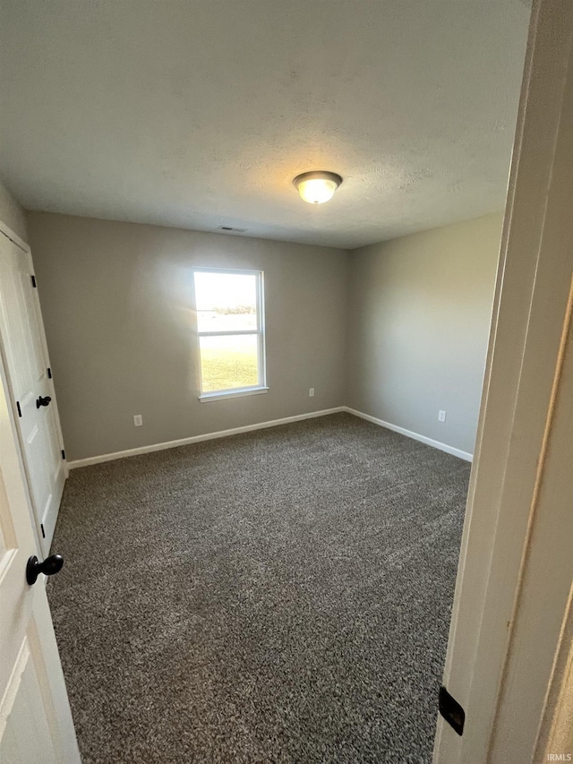 empty room with visible vents, baseboards, dark carpet, and a textured ceiling