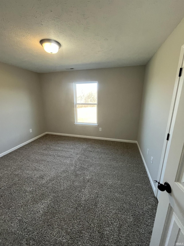 spare room featuring visible vents, a textured ceiling, baseboards, and dark colored carpet