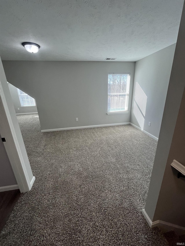 spare room featuring visible vents, carpet, baseboards, and a textured ceiling