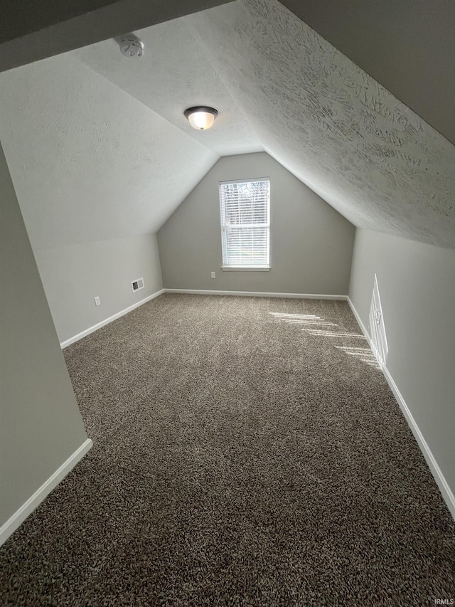 additional living space featuring visible vents, lofted ceiling, a textured ceiling, carpet flooring, and baseboards