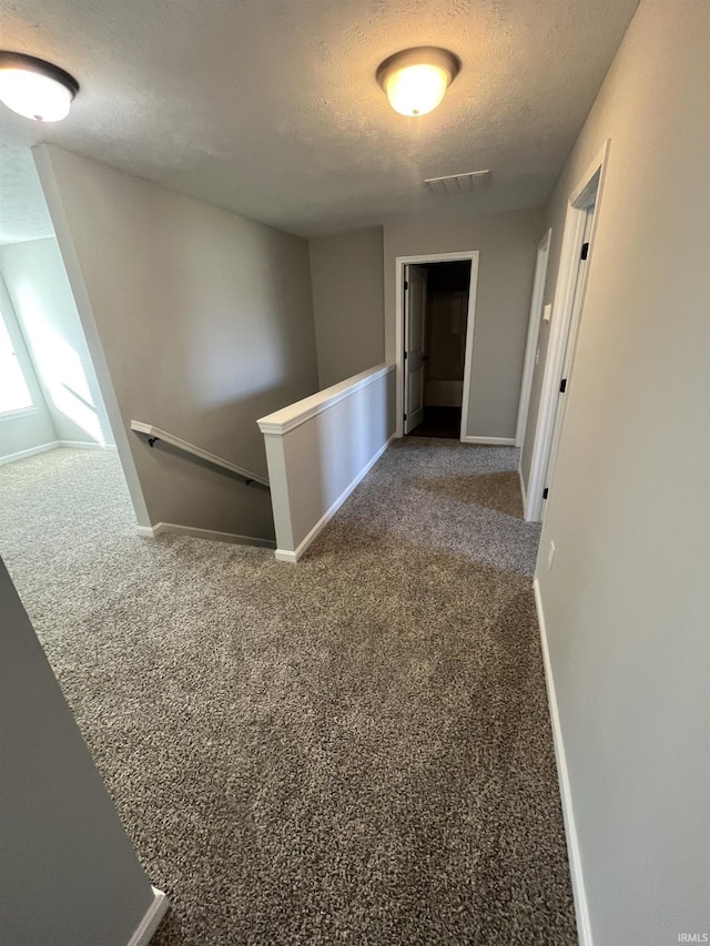 corridor with baseboards, visible vents, carpet floors, a textured ceiling, and an upstairs landing