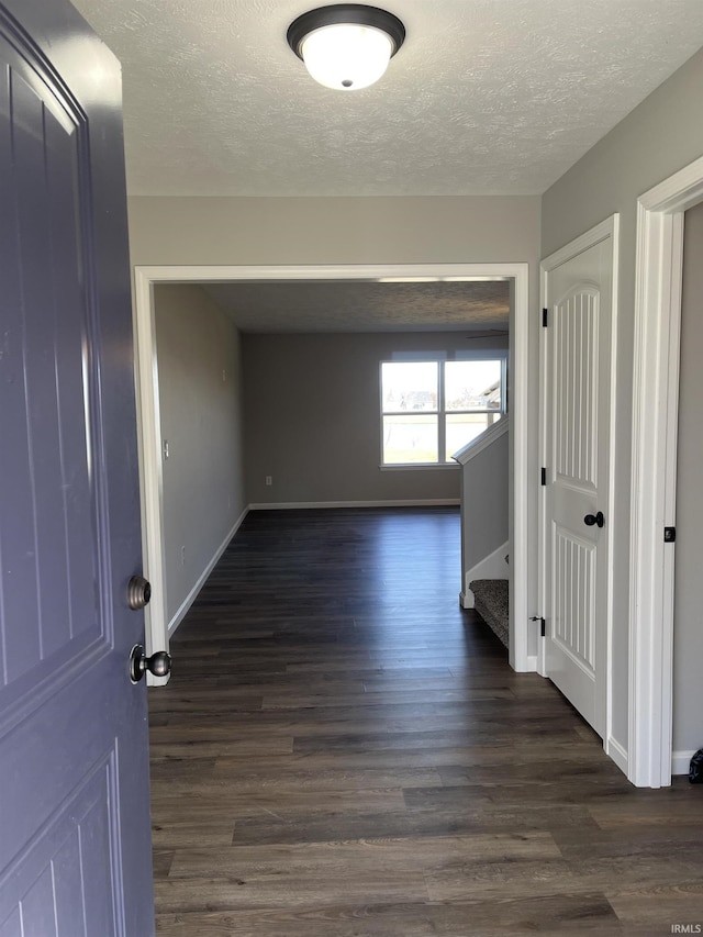 hallway with dark wood-style floors, a textured ceiling, stairs, and baseboards