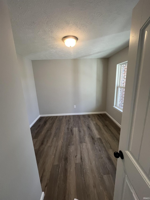 empty room featuring baseboards, a textured ceiling, and dark wood finished floors