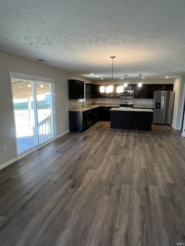 kitchen featuring a kitchen island, backsplash, dark wood finished floors, stainless steel appliances, and light countertops