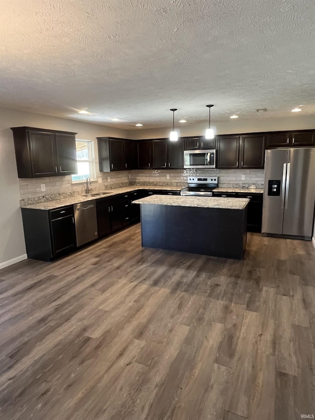 kitchen with a kitchen island, a sink, dark wood-type flooring, appliances with stainless steel finishes, and backsplash