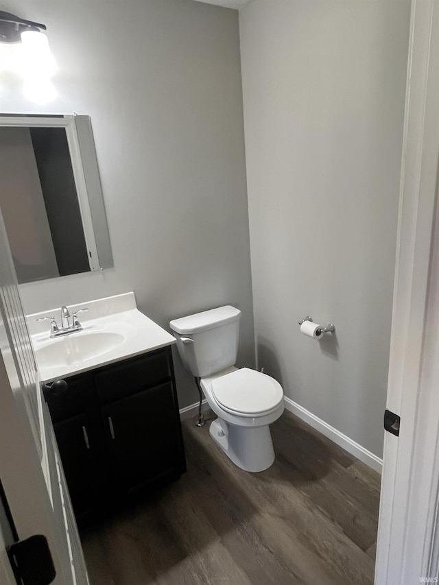 half bathroom featuring baseboards, toilet, wood finished floors, and vanity