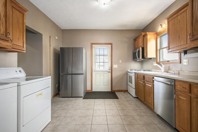 kitchen featuring washing machine and clothes dryer, a sink, light countertops, appliances with stainless steel finishes, and brown cabinets