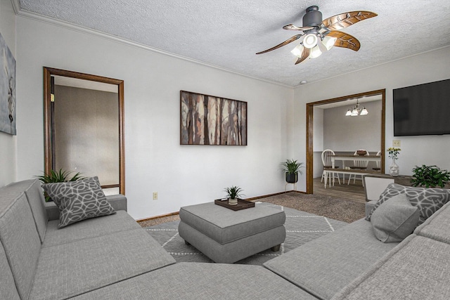 living room featuring ceiling fan with notable chandelier, a textured ceiling, baseboards, and ornamental molding