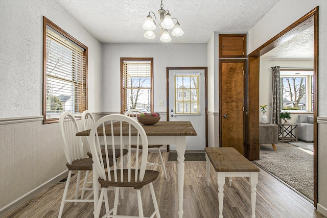 dining space featuring wood finished floors, a notable chandelier, a healthy amount of sunlight, and a textured ceiling