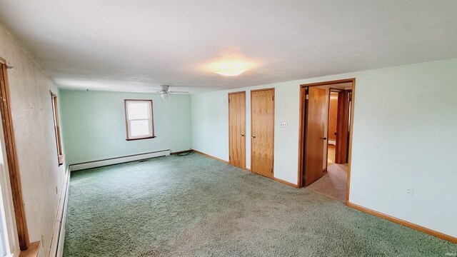 unfurnished bedroom with two closets, light colored carpet, baseboards, and baseboard heating