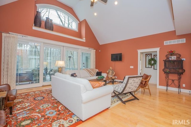 living area featuring light wood-type flooring, visible vents, baseboards, and high vaulted ceiling