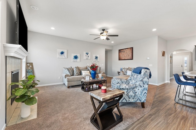 living room featuring arched walkways, recessed lighting, a tiled fireplace, and baseboards