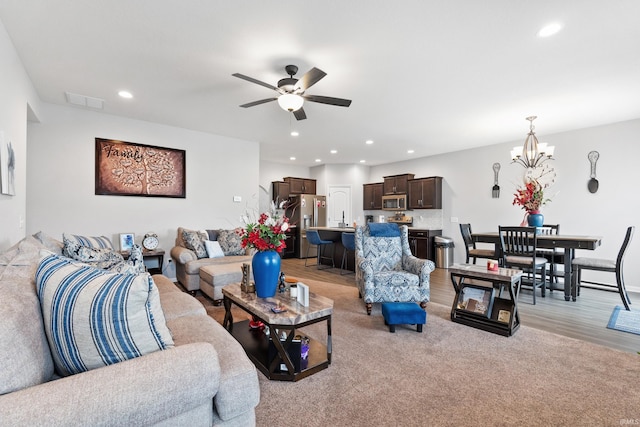 living area with recessed lighting, visible vents, light wood-type flooring, and ceiling fan with notable chandelier