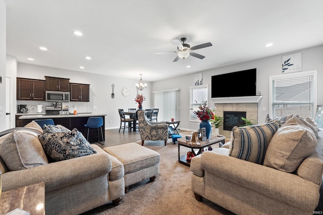 living room with recessed lighting, a tile fireplace, ceiling fan with notable chandelier, and baseboards