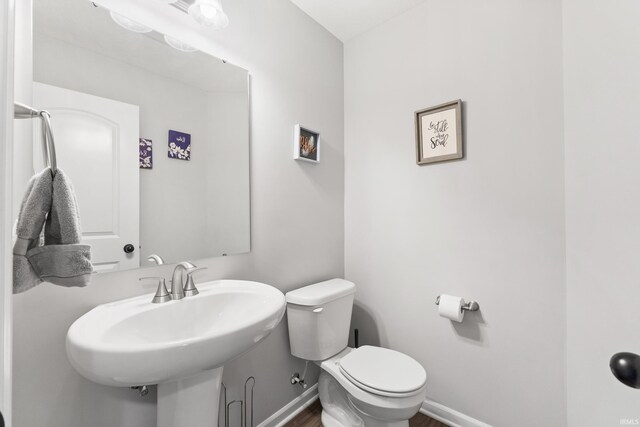 half bathroom with toilet, wood finished floors, baseboards, and a sink