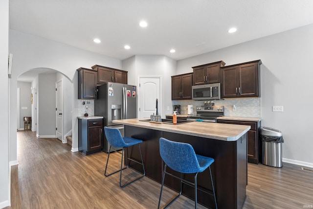 kitchen with arched walkways, dark brown cabinets, appliances with stainless steel finishes, and light countertops