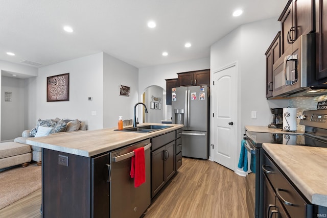 kitchen with light wood-style flooring, a sink, open floor plan, arched walkways, and appliances with stainless steel finishes